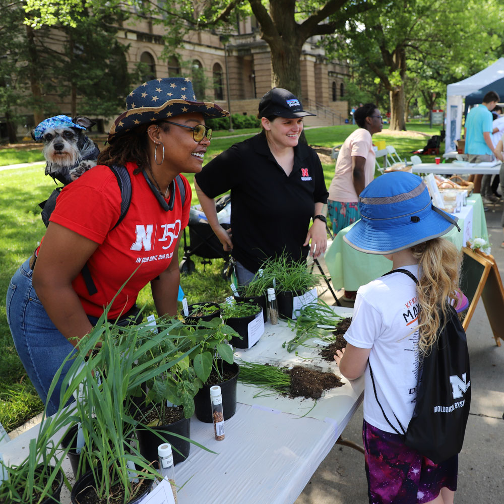 Bellodgia Roberson with her dog Charlie (left), and Bridget McKinley, both agronomy graduate students, help visitors explore various types of cover crops at the Agronomy and Horticulture booth during the East Campus Discovery Days and Farmers Market June 8. 