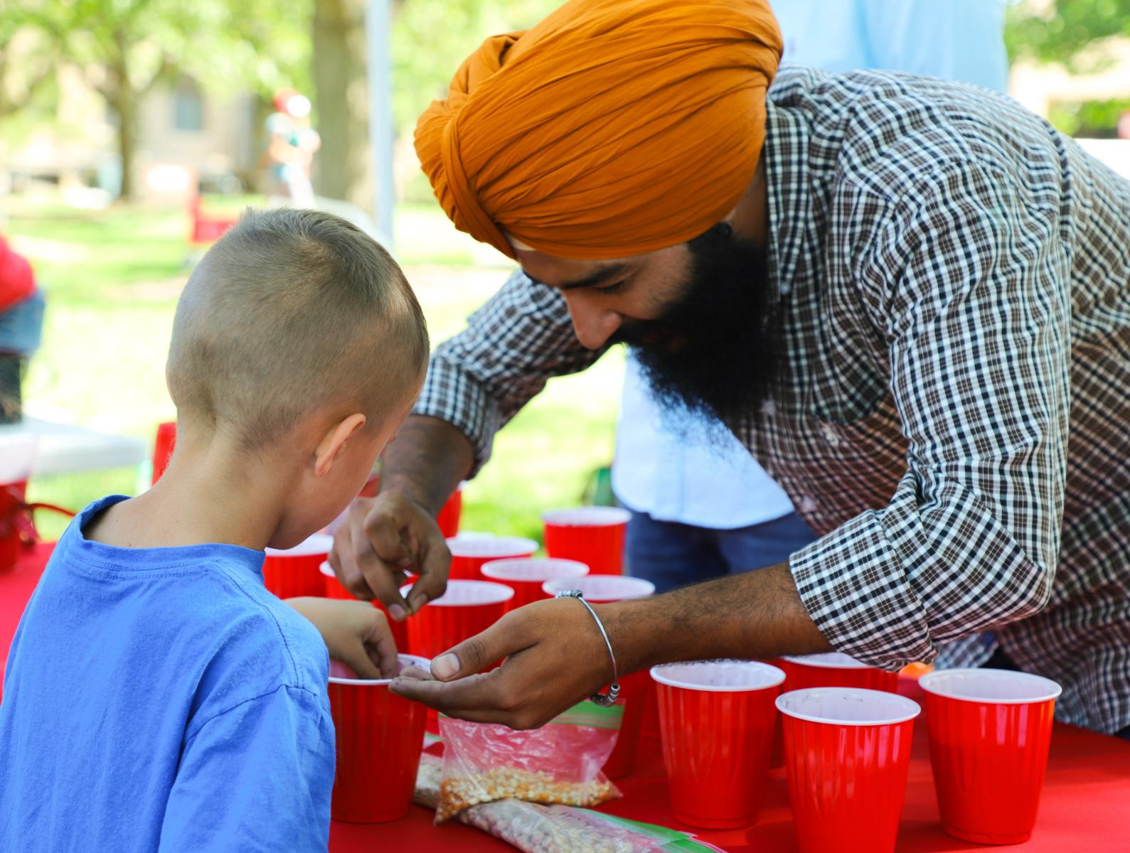 Mandeep Singh, doctoral student in the Department of Agronomy and Horticulture, helps a future scientist plant seeds in a cup of soil at the Plant a Seed booth during East Campus Discovery Days and Farmers Market 