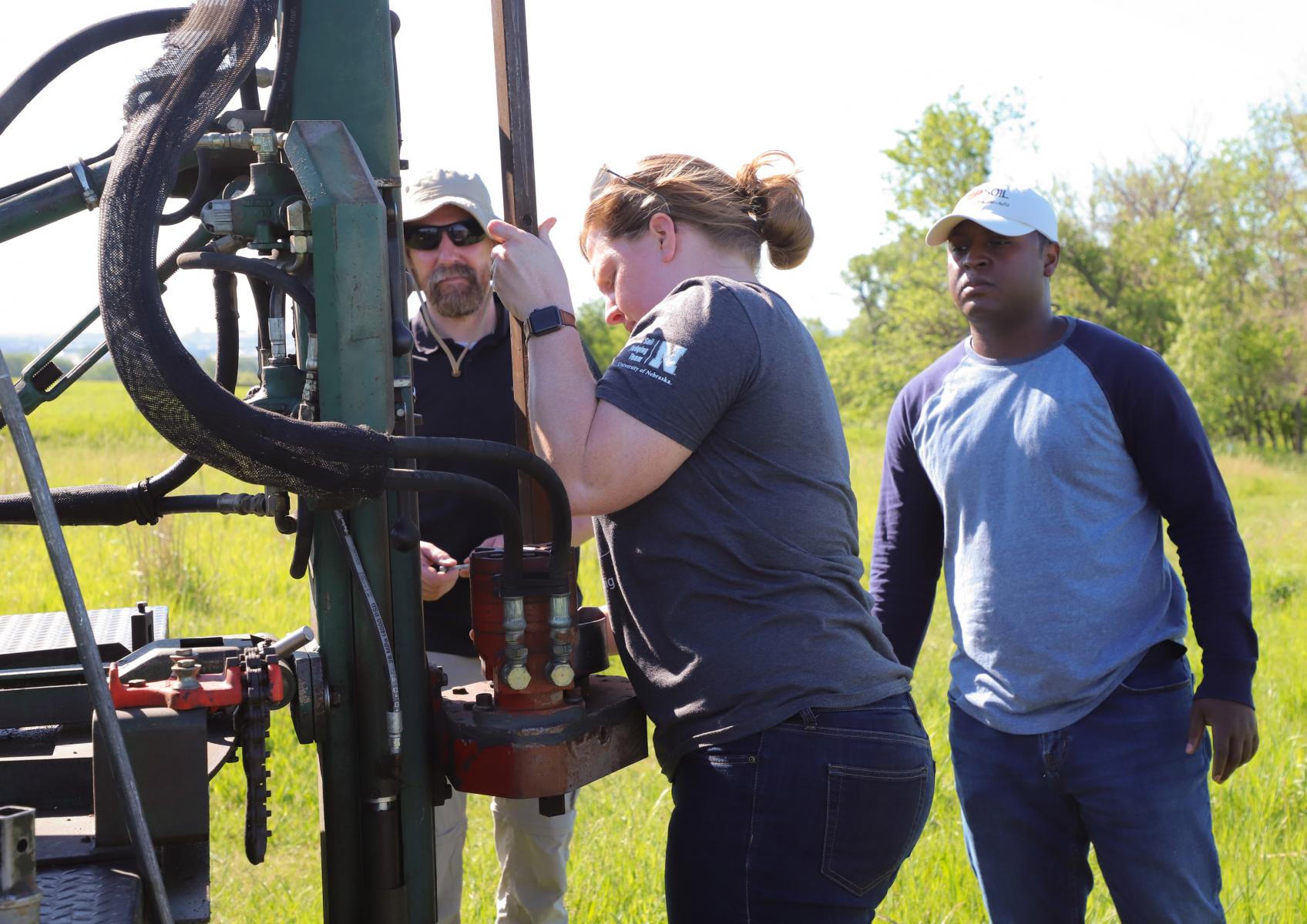 Rebecca Young, Department of Agronomy and Horticulture assistant professor of practice, demonstrates for agronomy assistant professor Michael Kaiser, left, and Christopher Anuo, agronomy doctoral student, proper use of a truck-mounted hydraulic soil probe in collecting soil cores at Nine-Mile Prairie for use in Agronomy 153 Soil Resources classes.
