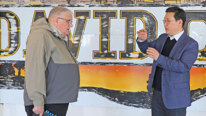 Two people speak in front of a mural speling out David.