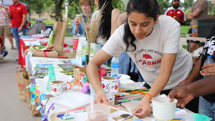 Woman engaging in a craft activity at an outdoor event table with colorful materials.