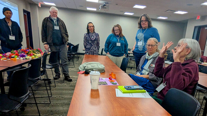 Group of people in a conference room with materials on a table, engaging in discussion.