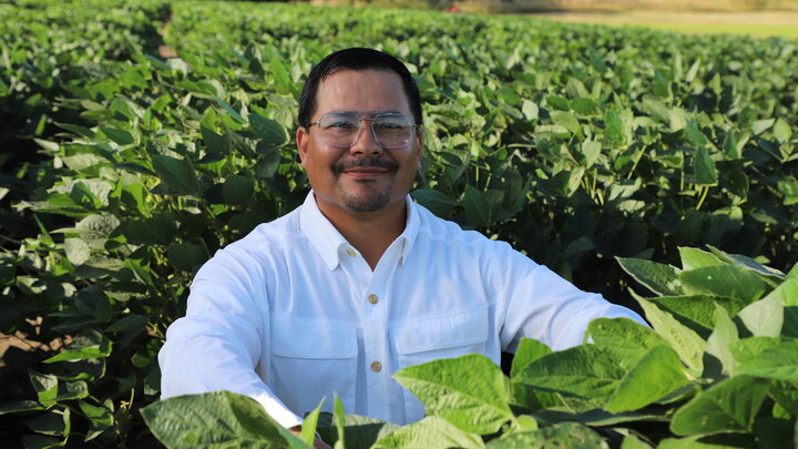Luis Posadas Martinez sits in a field of soybeans and smiles at the camera