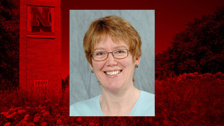 A woman with short hair over a red background featuring a University of Nebraska emblem.
