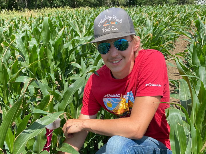 Austin Kamm crouches in a field and smiles at the camera