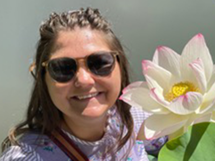 Cecile Renfro poses for a picture with a large white flower with pink-tipped petals and a yellow center