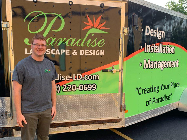 Brandon Mars poses in front of a Paraides Landscape and Design company trailer