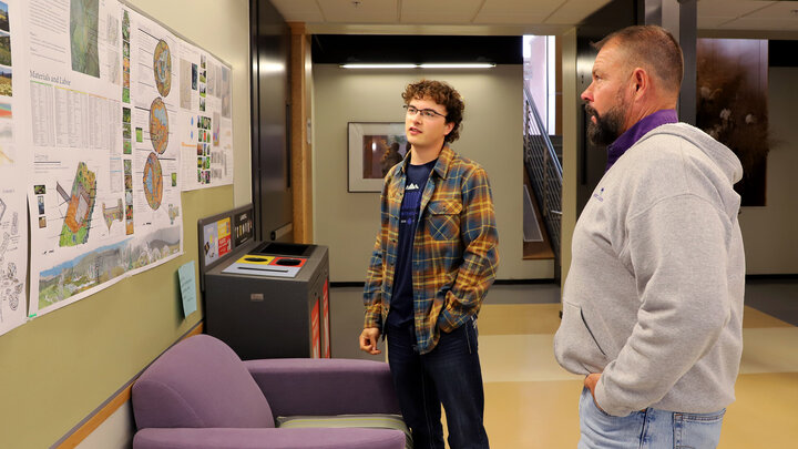 Two people standing in a hallway, looking at colorful posters on the wall.