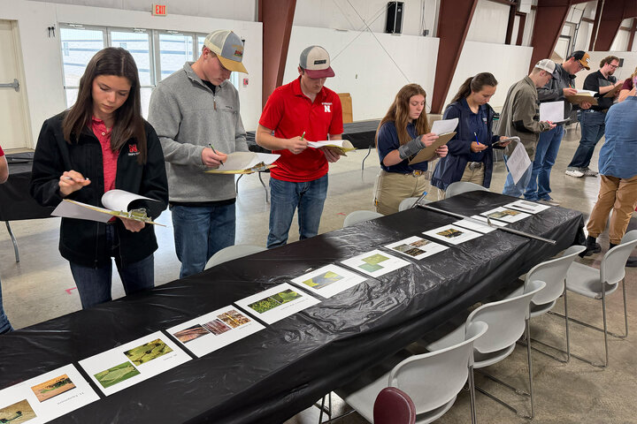 Group of people examining agricultural materials on a long table in a large indoor setting.