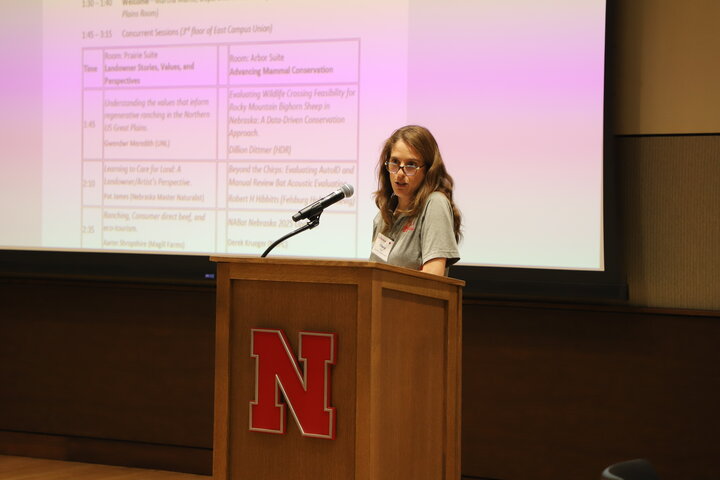 Cheryl Dunn stands behind a wooden lectern with a red N on the front of it as she speaks to conference attendees.