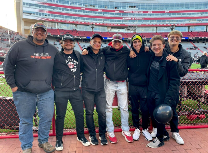 Seven people stand together near a football stadium, dressed casually in jackets and jeans.