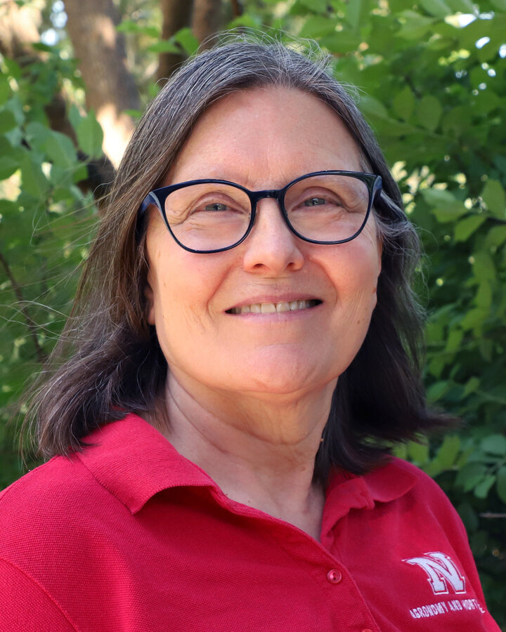 Person wearing a red polo shirt with a logo, standing outdoors near green foliage.