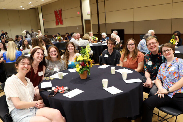 Guests seated at round tables with floral centerpieces during a social event in a banquet hall.